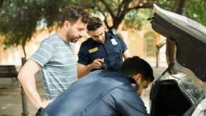 Driver looks on as police complete a search of his motor vehicle's trunk.