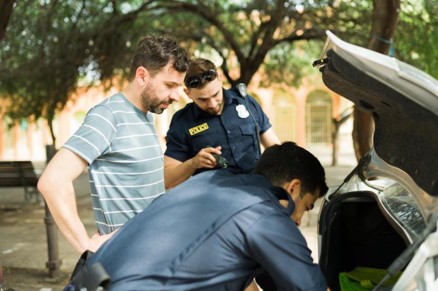 Driver looks on as police complete a search of his motor vehicle's trunk.