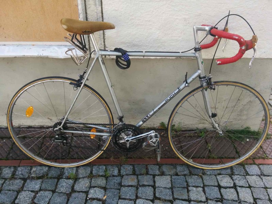 Silver Puch road racing bicycle leaned against a wall on a cobblestone street.