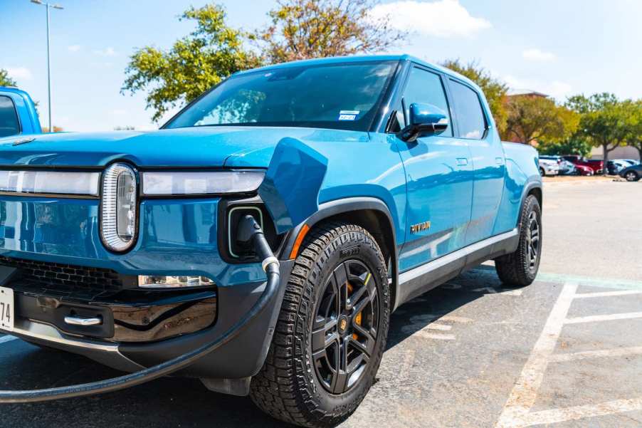 blue electric Rivian truck plugged into a charging cable.