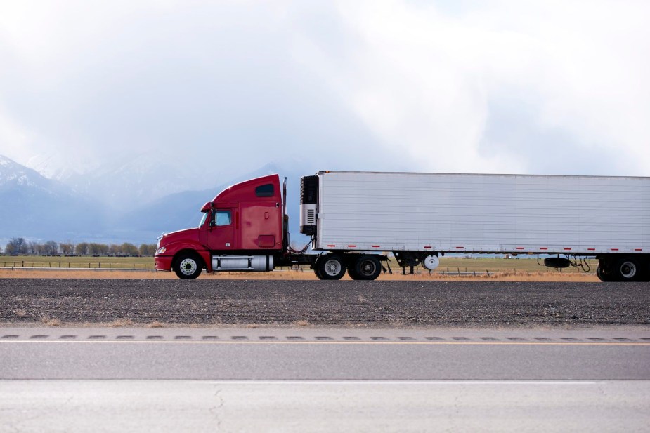 Red semi truck towing a refrigerated trailer down the highway.