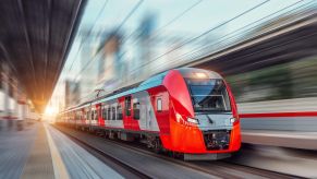 A brightly colored express train speeds past the platform in a station.