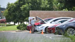 Man holds up the hood on the front trunk of a Tesla at a charging station.