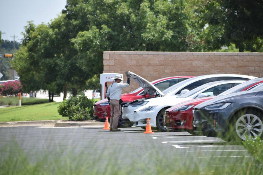 Man holds up the hood on the front trunk of a Tesla at a charging station.