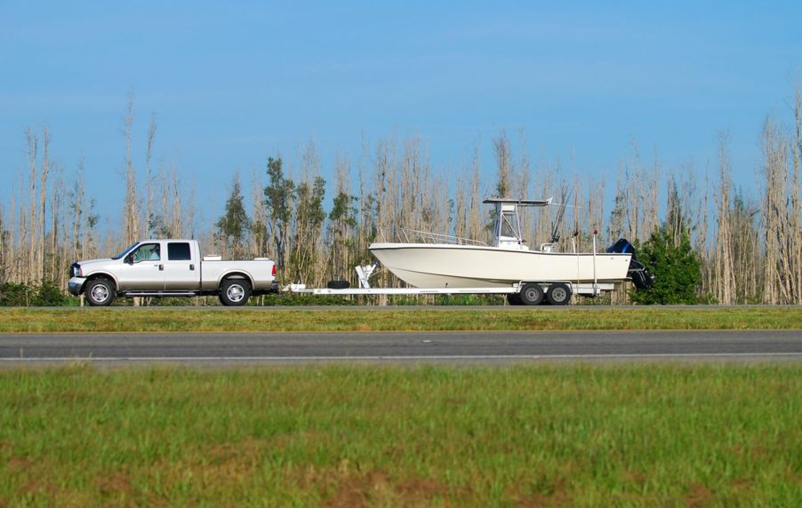 A white truck towing a trailer with a boat.