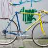 Vintage blue and yellow Peugeot road racing bicycle leaned against a graffiti-covered wall.