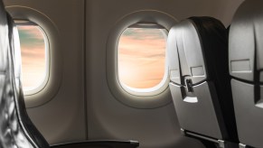 View of airplane window from inside passenger cabin showing airplane seats in close view