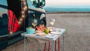 A compact dinner setting on a foldable table while car camping includes wine glasses, fruit, salad, bread, and more