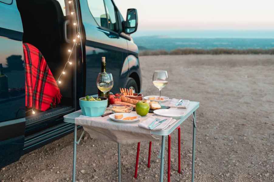 A compact dinner setting on a foldable table while car camping includes wine glasses, fruit, salad, bread, and more