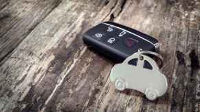 A black car key fob with a silver metal car cutout keychain sitting on a distressed wood surface