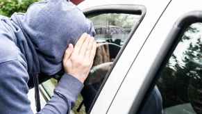 man in blue hoodie face covered peering into car window in close view hand covering side of face depicting car theft