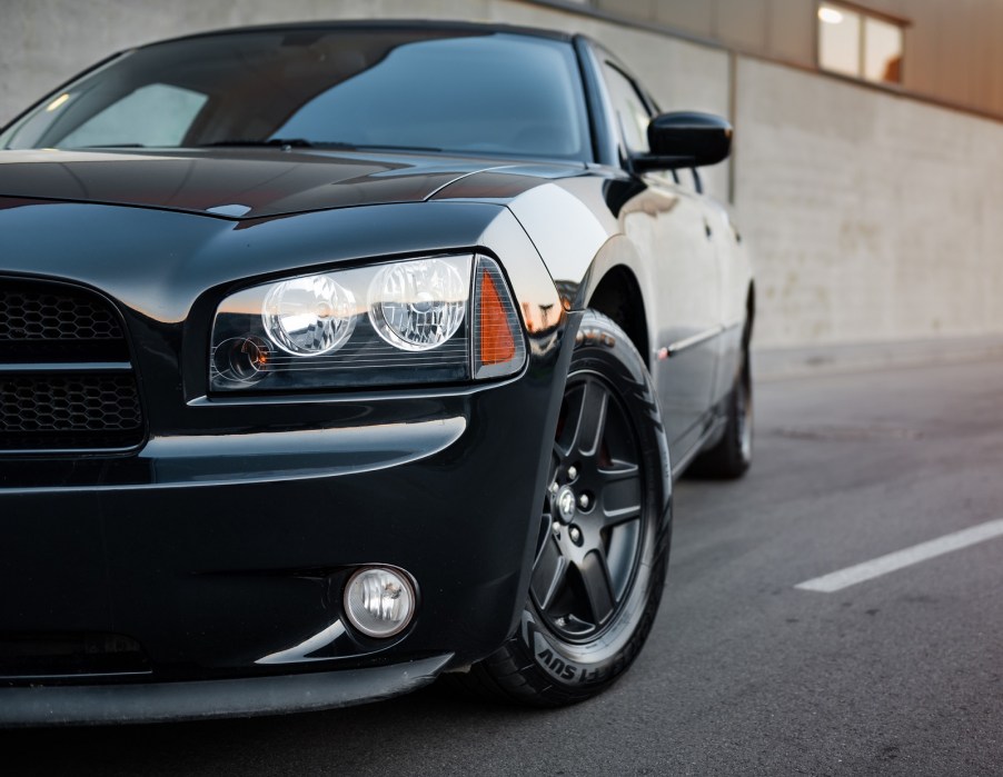 A black Dodge Charger muscle car parked on a paved road in left front angle view showing the left front corner