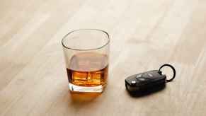 A depiction of a DUI via a car key fob and glass of whiskey on the rocks on a light wood surface