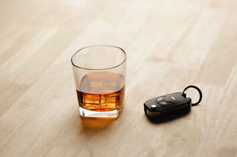 A depiction of a DUI via a car key fob and glass of whiskey on the rocks on a light wood surface