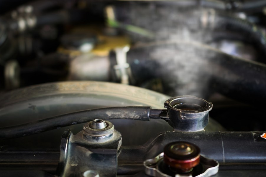 An overheating engine has steam coming out of the top of the radiator, the cap is off and sitting upside down