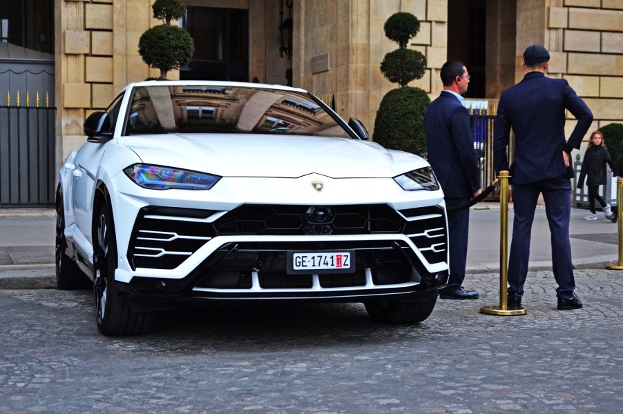 A white Lamborghini Urus SUV parked in slight right front angle view with two suited men standing facing away from the driver's side