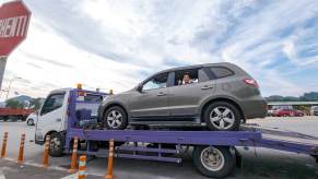 Passenger gives the thumbs up from inside a car on a tow trailer