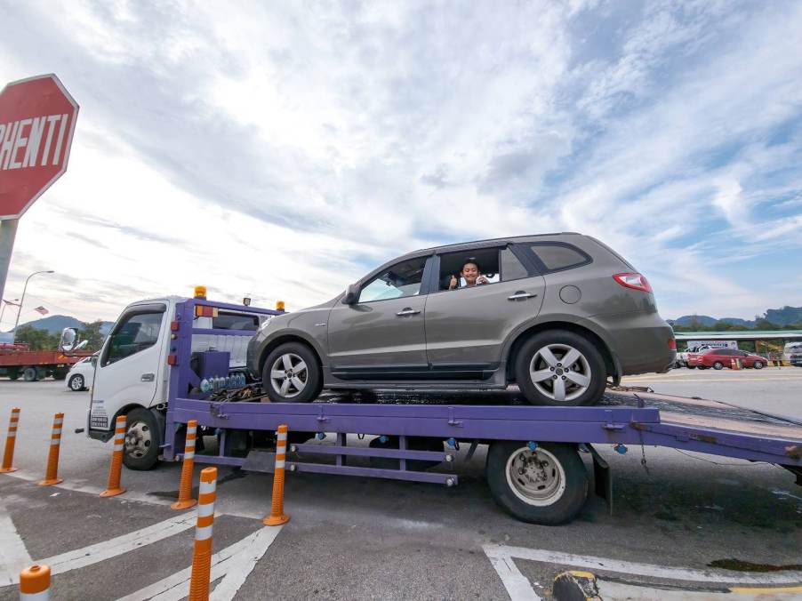 Passenger gives the thumbs up from inside a car on a tow trailer