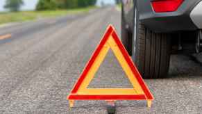 Close up depiction of a car breakdown with an orange road triangle in front center and vehicle parked behind depiction of roadside assistance needed