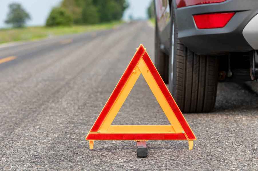 Close up depiction of a car breakdown with an orange road triangle in front center and vehicle parked behind depiction of roadside assistance needed