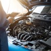 A mechanic performs a vehicle maintenance inspection on a blue car with hood open using an iPad