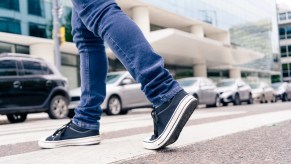 Depiction of stranger's legs wearing jeans and sneakers crossing the street approaching cars.