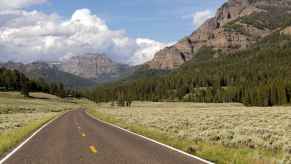 Road in Yellowstone National Park with mountains and trees in midground if you have a remote car breakdown you should have food and water in your car