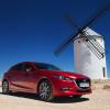 Bright red Mazda3 wagon parked in front of a windmill, the Spanish countryside visible behind it.