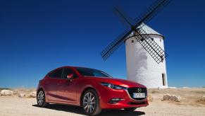 Bright red Mazda3 wagon parked in front of a windmill, the Spanish countryside visible behind it.