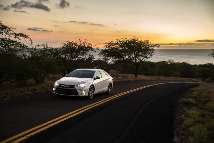 A 2015 Toyota Camry XLE drives around a corner under a sunset.