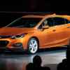 A rust-orange 2017 Chevrolet Cruze hatchback parked on a stage in full left and side angle view