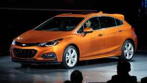 A rust-orange 2017 Chevrolet Cruze hatchback parked on a stage in full left and side angle view