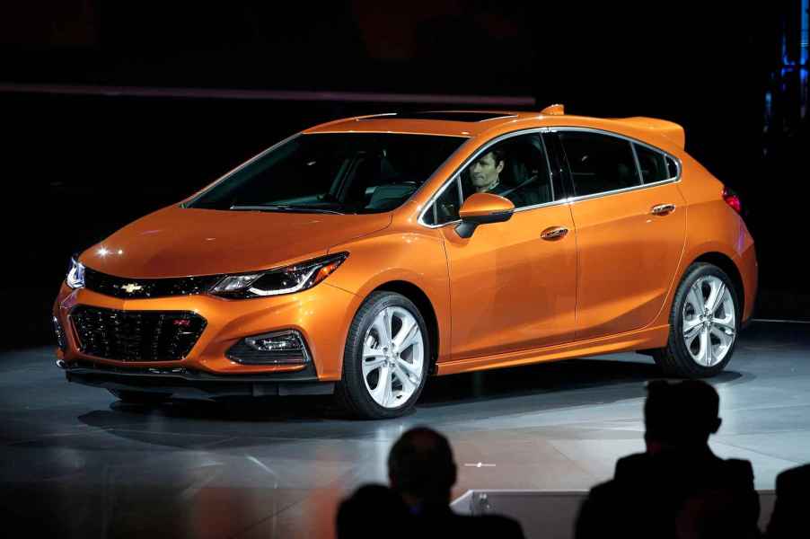 A rust-orange 2017 Chevrolet Cruze hatchback parked on a stage in full left and side angle view