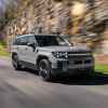 A flat grey 2024 Hyundai Santa Fe midsize SUV crossover driving on a paved road in front of a rocky mountain