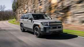 A flat grey 2024 Hyundai Santa Fe midsize SUV crossover driving on a paved road in front of a rocky mountain