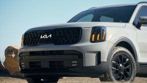 A matte gray 2024 Kia Telluride parked in left front angle view front end and part of left door