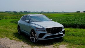 Gray crossover SUV with a coupe fastback parked in a field, trees visible in the background.