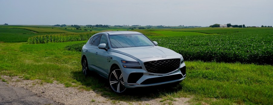 Gray crossover SUV with a coupe fastback parked in a field, trees visible in the background.