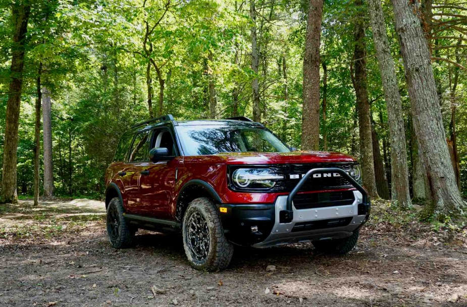 Red Ford Bronco Sport AWD crossover parked in the woods, trees visible in the background.