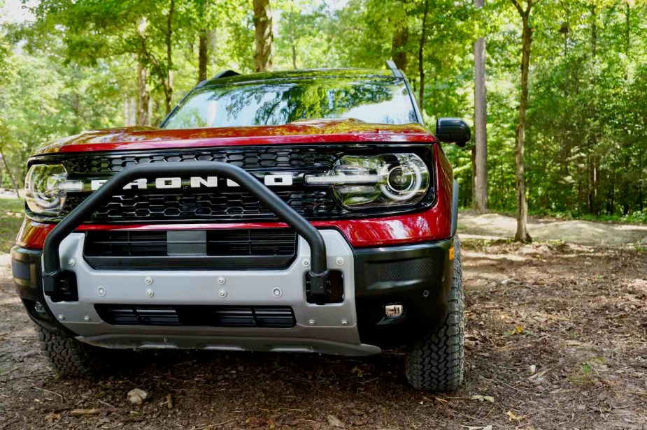 Red Ford Bronco Sport with a 'Sasquatch package' brush guard parked in the woods, trees visible in the background.