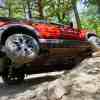 Red 2025 Bronco Sport Badlands shows off its 29-inch Goodyear tires by lifting one in the air as it crawls over rocks, trees visible in the background.