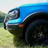 The 29-inch Goodyear tires on the front of a blue 2025 Bronco Sport with the Sasquatch package, a lake visible in the background.