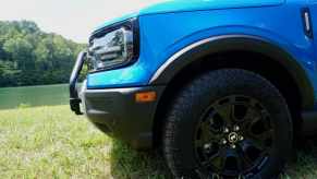 The 29-inch Goodyear tires on the front of a blue 2025 Bronco Sport with the Sasquatch package, a lake visible in the background.