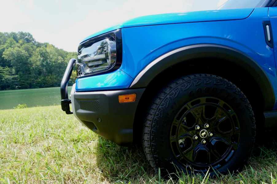 The 29-inch Goodyear tires on the front of a blue 2025 Bronco Sport with the Sasquatch package, a lake visible in the background.