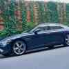 Dark green Genesis luxury sedan parked in front of a vine covered wall.