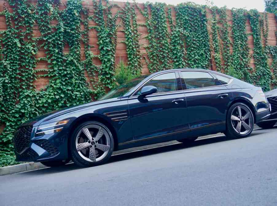 Dark green Genesis luxury sedan parked in front of a vine covered wall.