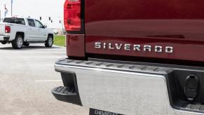 The Silverado badge on the tailgate of a red Silverado pickup truck.