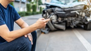 Driver sits next to a crashed car while making a phone call.