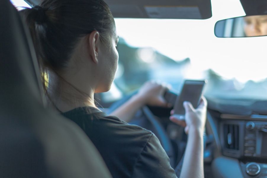 A teenage driver behind the wheel with cell phone in-hand.