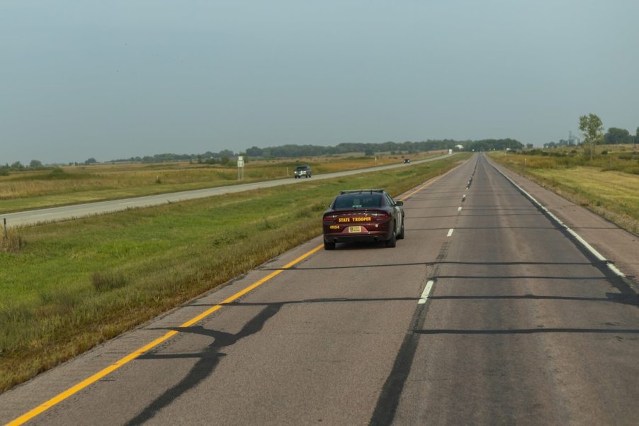 A camera vehicle following a police officer in a state trooper Dodge Charger on the highway.